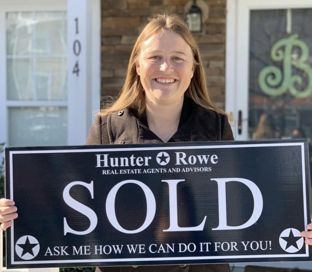 A satisfied Relevate client smiles while holding a "Sold" sign