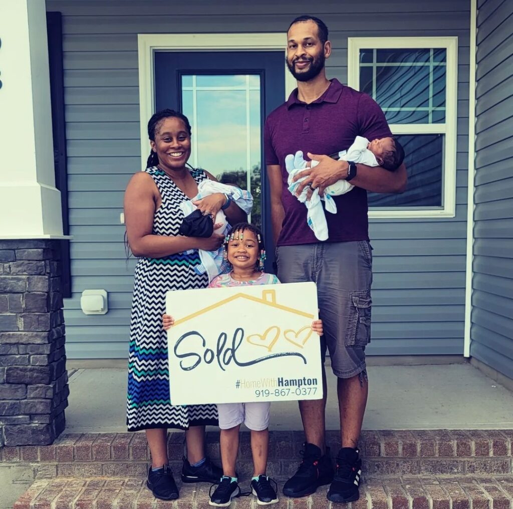 Family stands in front of home holding a sold sign