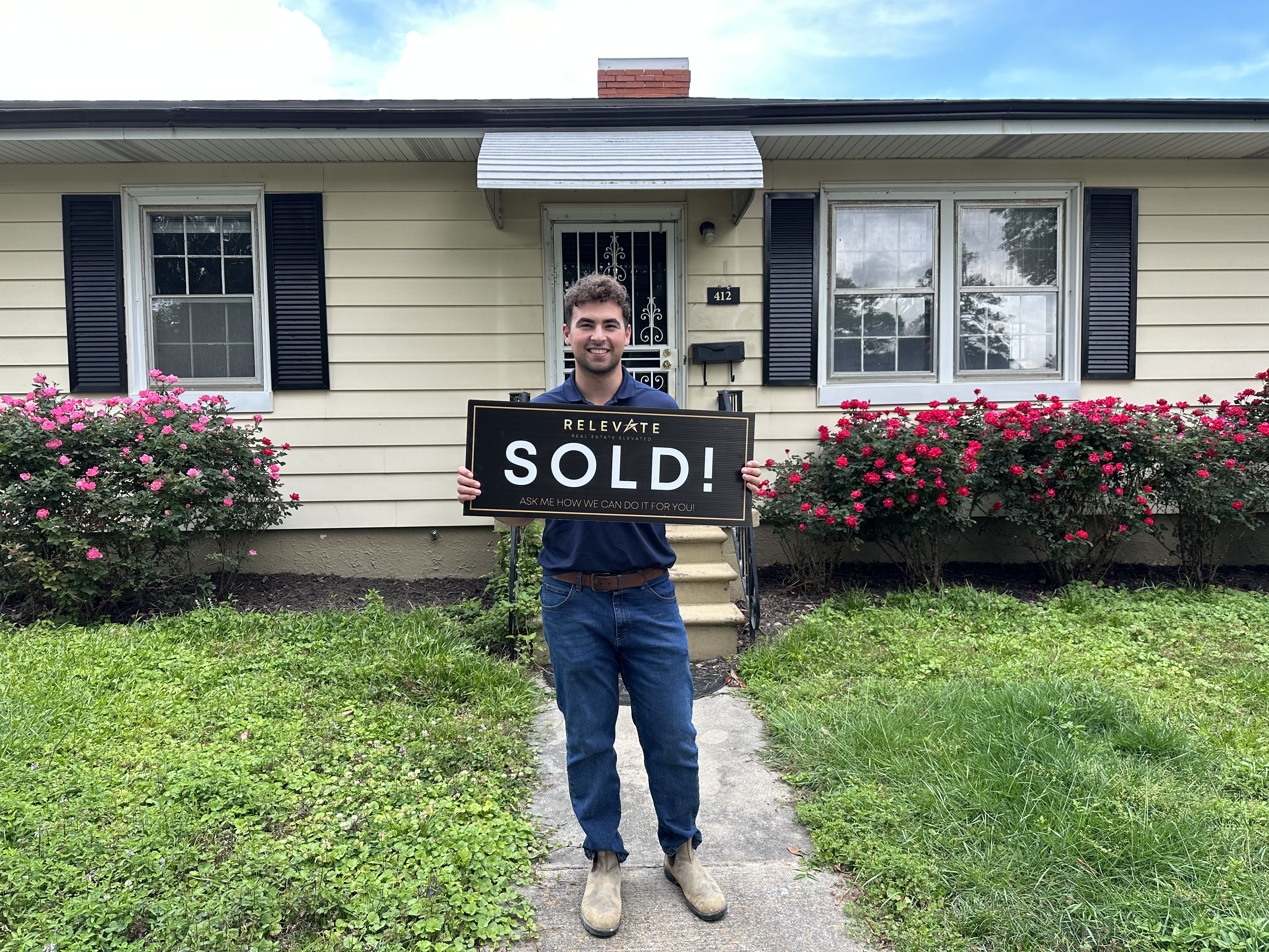Satisfied homebuyer stands in front of home with SOLD sign
