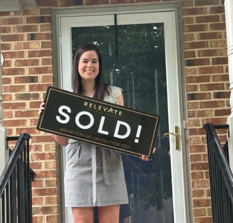 Happy young woman holding a for sold sign in front of her new home