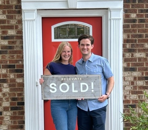 two happy people holding a sold sign in front of their new home