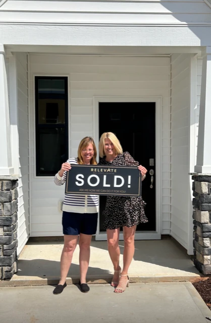 Agent and her client holding a sold sign in front of her new house.
